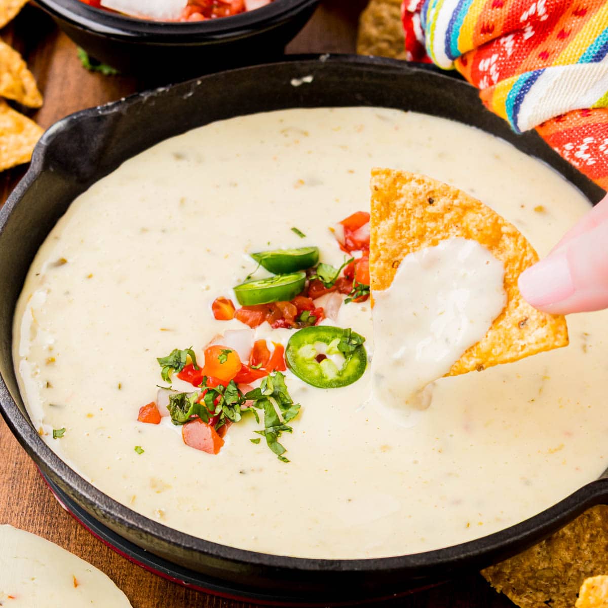 Hand dipping a chip into a skillet of white queso.