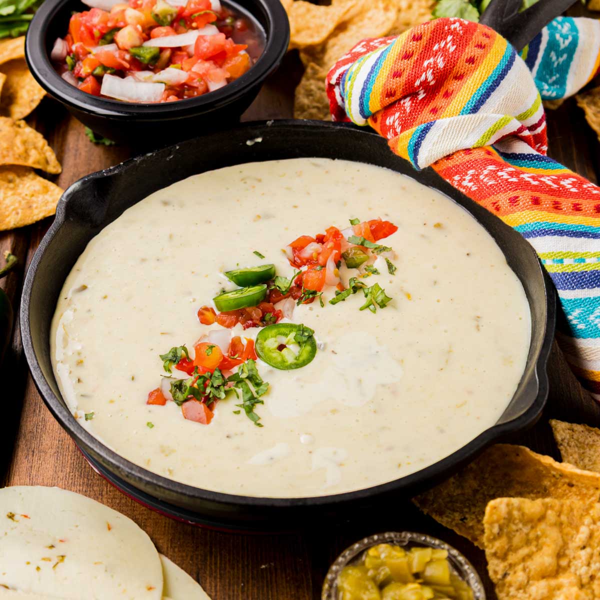 Cast iron skillet of white queso garnished with tomatoes and jalapenos.